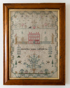 Framed sampler with embroidered design of a house and various elements on a white background
