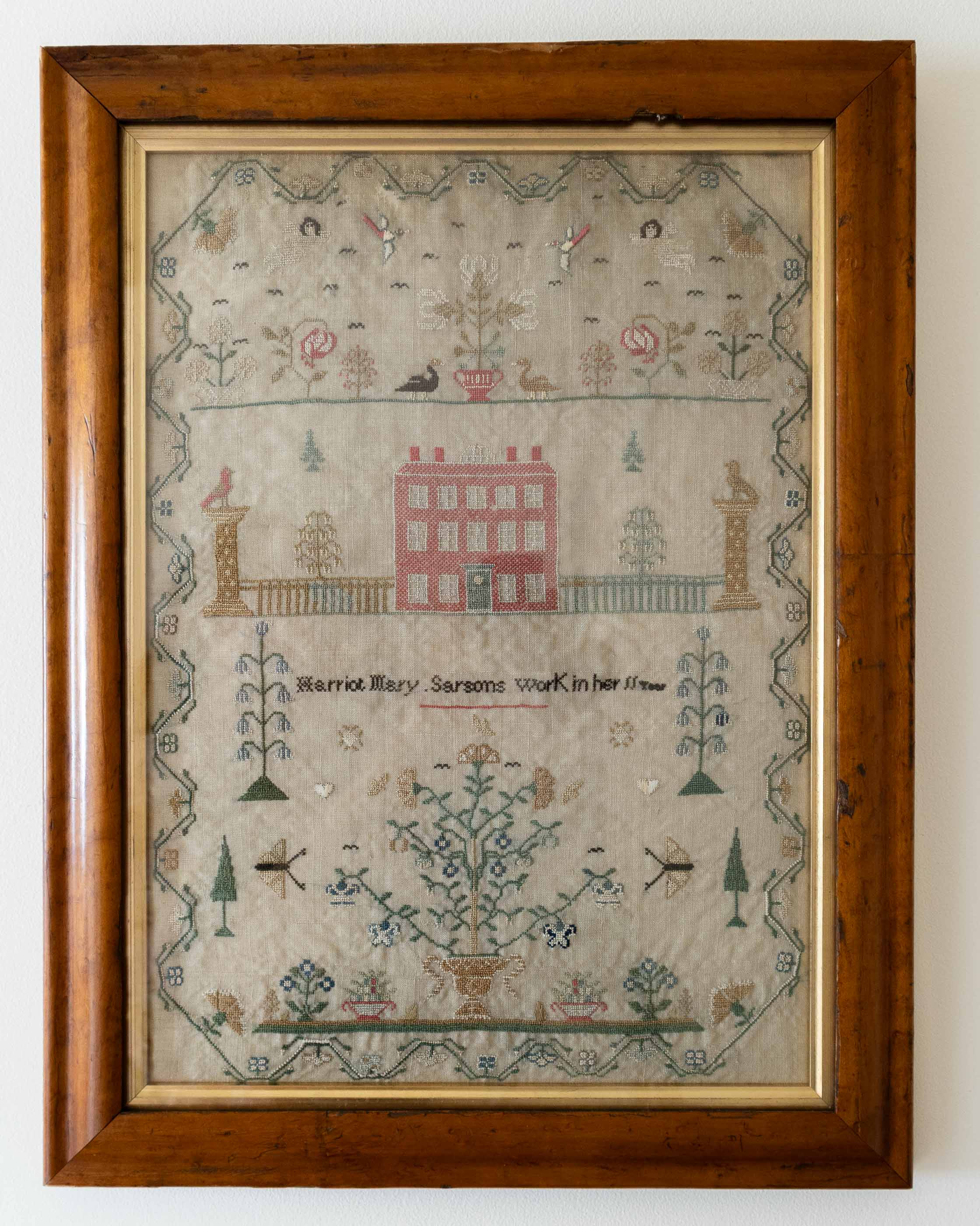 Framed sampler with embroidered design of a house and various elements on a white background