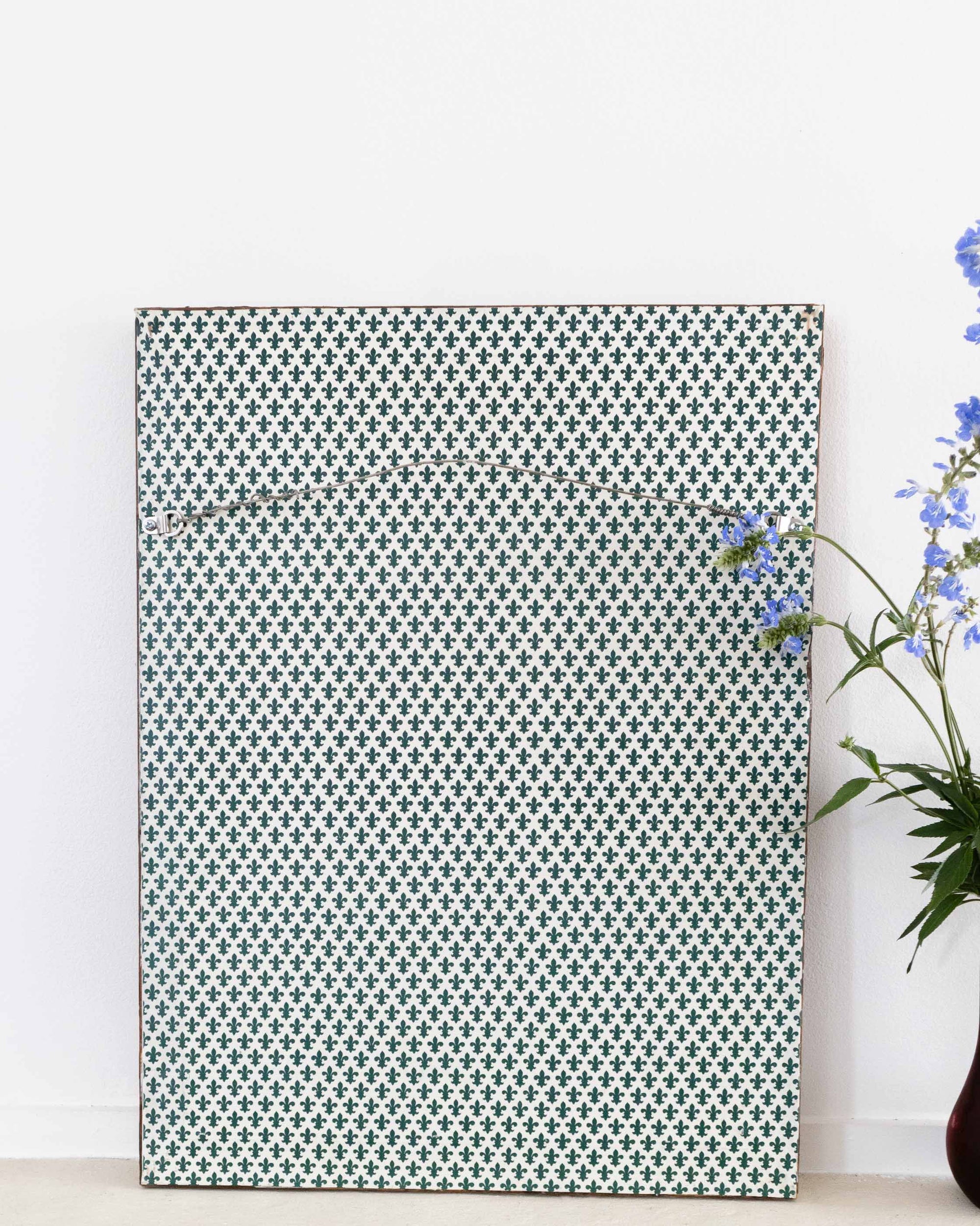 Patterned wall art piece on a white wall with a vase of flowers to the right.