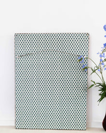 Patterned wall art piece on a white wall with a vase of flowers to the right.