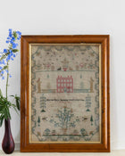 Framed sampler with decorative elements on a white wall