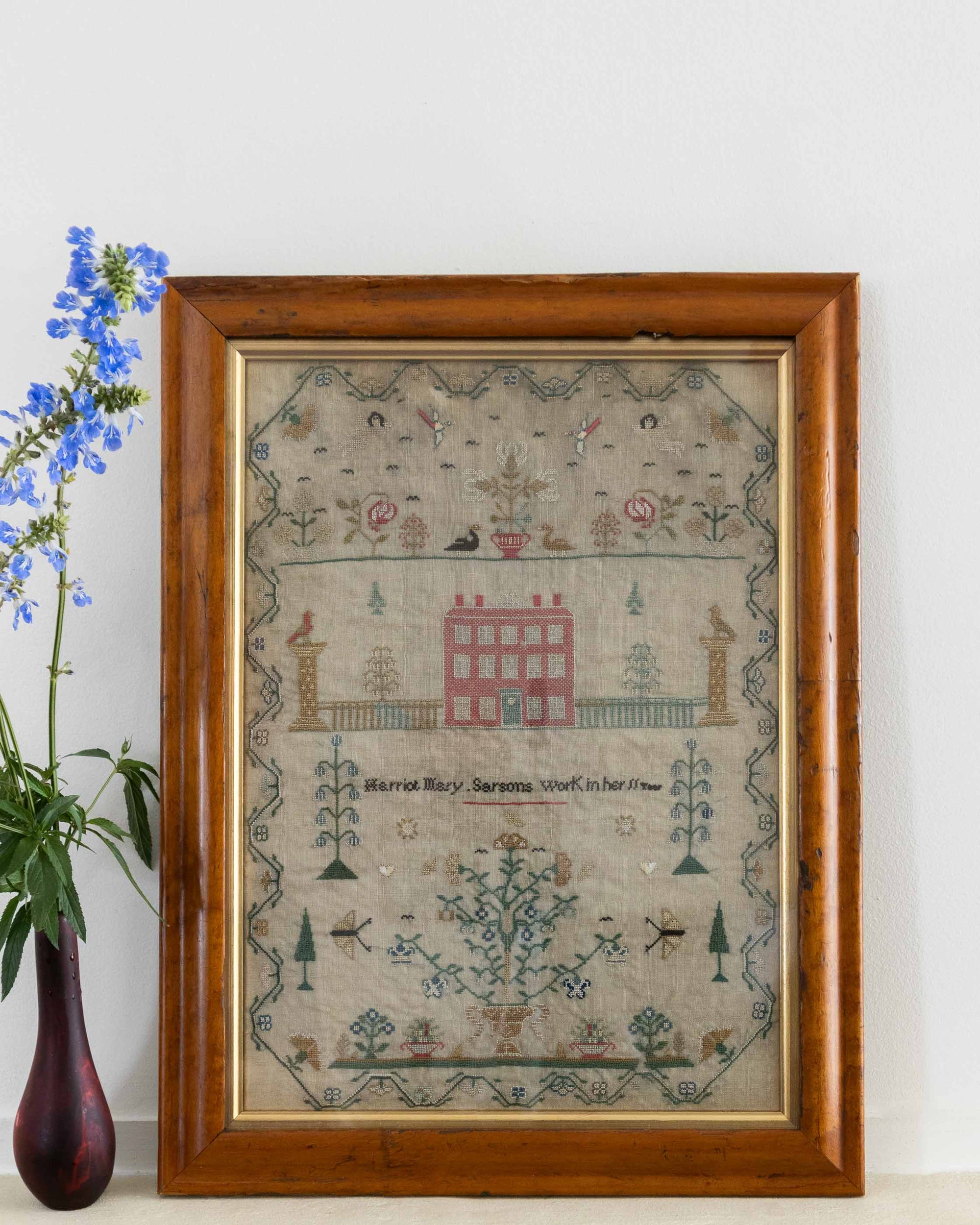 Framed sampler with decorative elements on a white wall