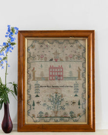 Framed sampler with decorative elements on a white wall