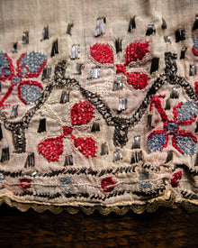 Close-up of embroidered fabric with red flowers, black and gray patterns on a beige background