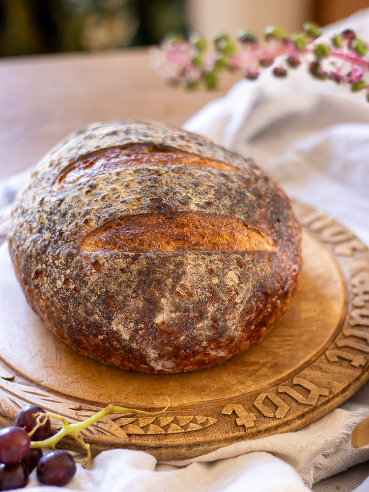Loaf of bread on a wooden breadboard with grapes and flowers in the background