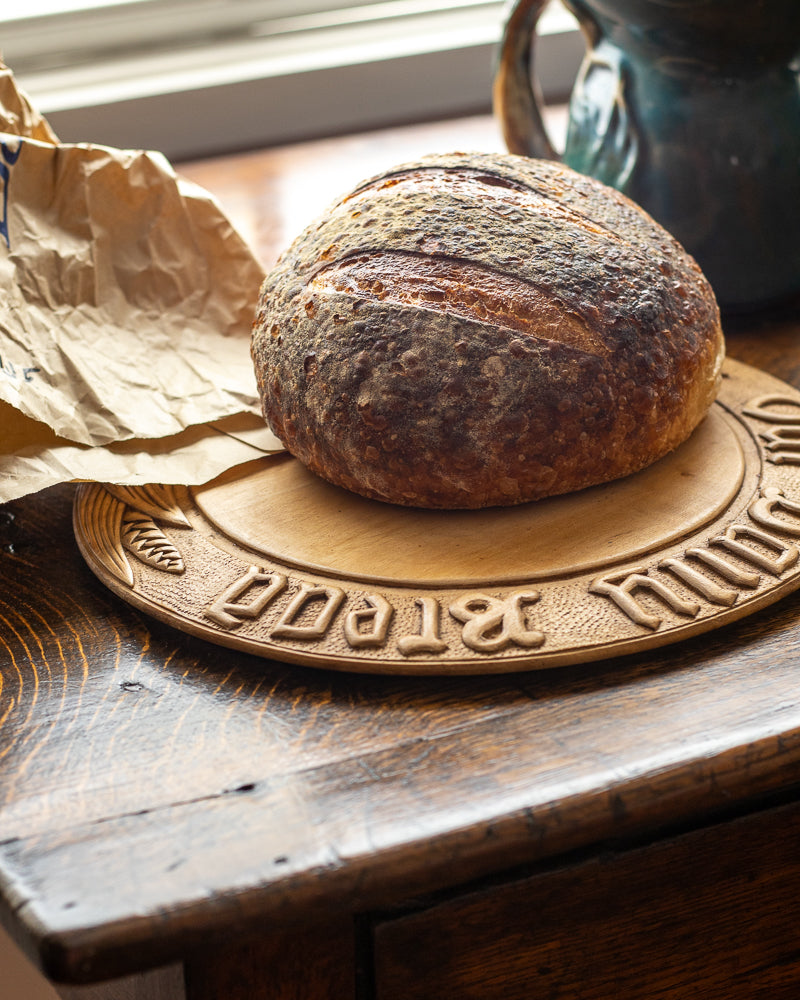 Loaf of bread on a wooden board with  carving on a rustic wooden surface.