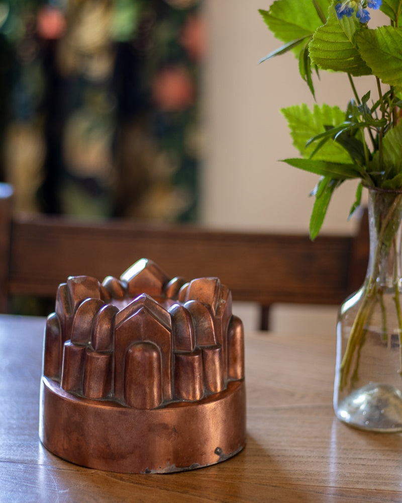Copper mold on a wooden table with a vase of flowers in the background
