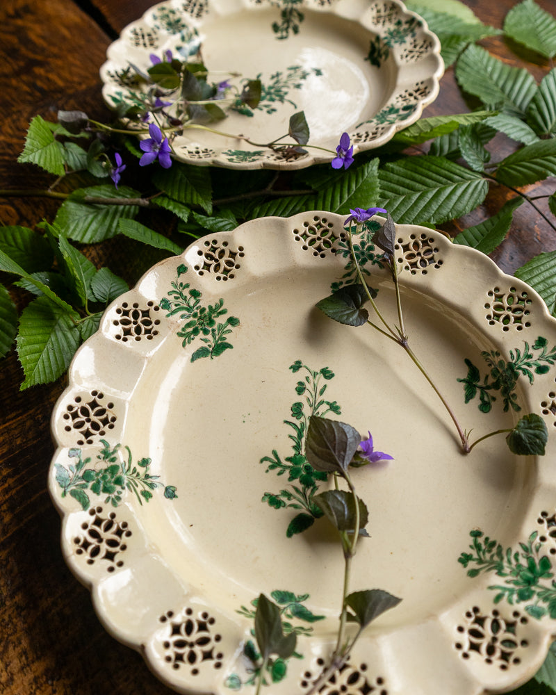 Antique creamware plates with floral patterns on a wooden surface with leaves and flowers.