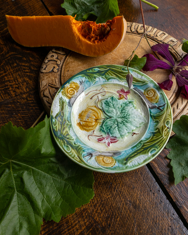 Decorative majolica plate with floral design on a wooden surface with a halved pumpkin and leaves.