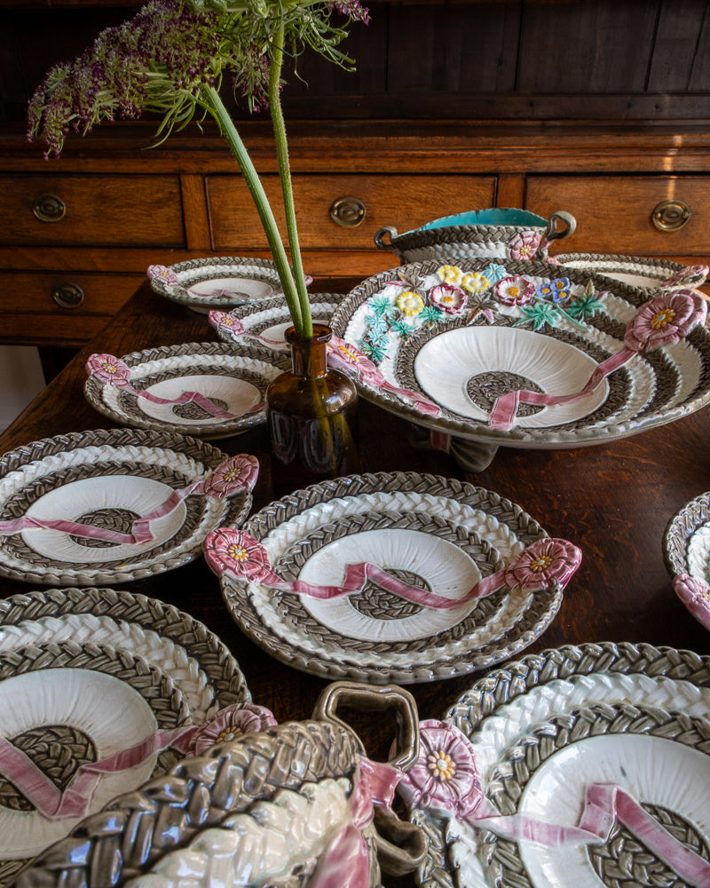 Antique majolica plates with floral and ribbon designs on a wooden table.