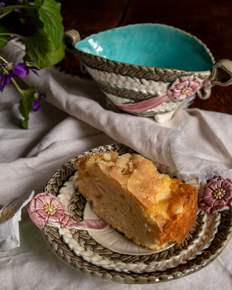 Slice of apple pie on a decorative plate with a woven design, placed on a textured surface.