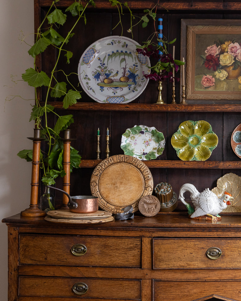 Antique dresser with decorative plates, teapot, and other items on a wooden shelf.