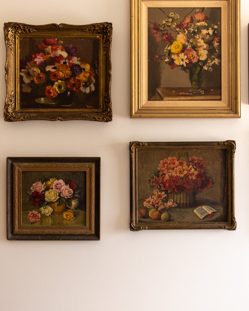 Four framed paintings of floral still lifes on a white wall.