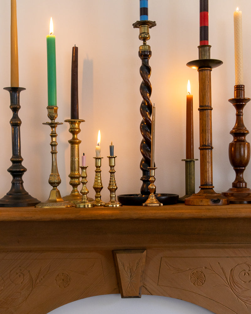 Collection of candles in various candlesticks on a wooden surface with a neutral background