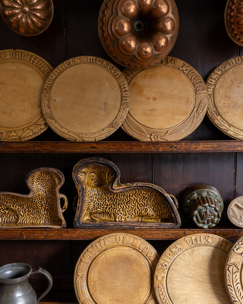 Collection of wooden breadboards and copper molds on a wooden shelf with a dark background