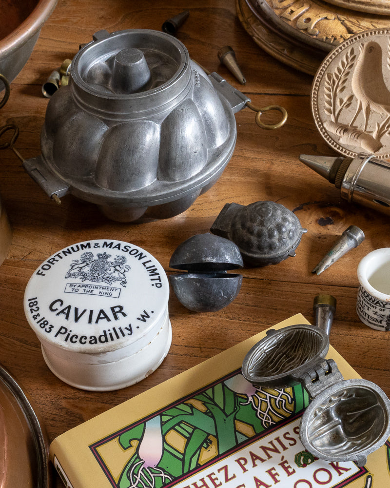 Collection of vintage kitchen items including a caviar container and metal molds on a wooden surface.