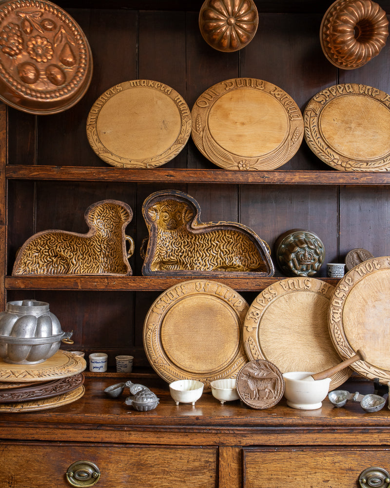 Collection of wooden and metal kitchen utensils on a wooden shelf against a dark wooden wall.