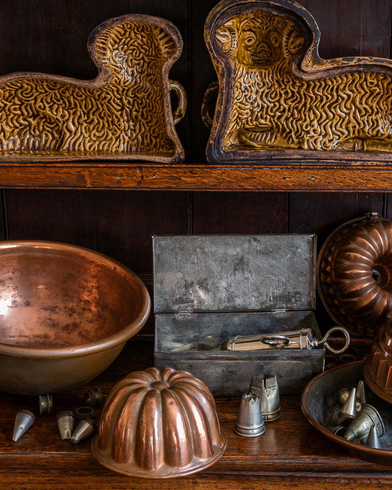 Collection of antique copper and metal kitchen utensils on a wooden shelf.