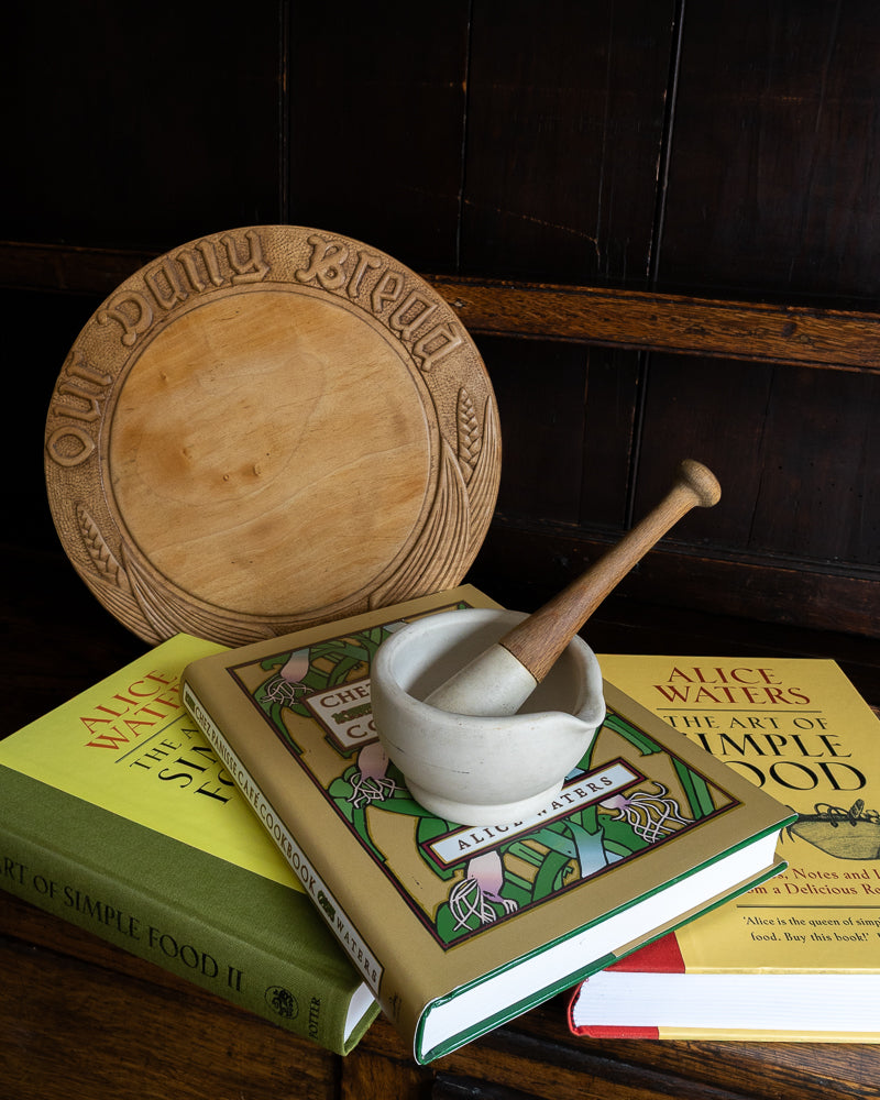 Wooden breadboard and mortar and pestle on a stack of cookbooks.