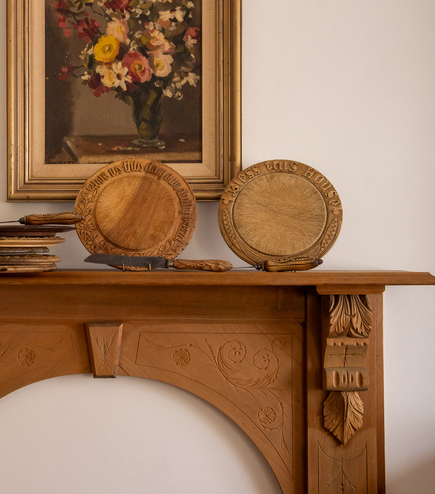 Wooden decorative items on a wooden mantelpiece with a painting in the background.