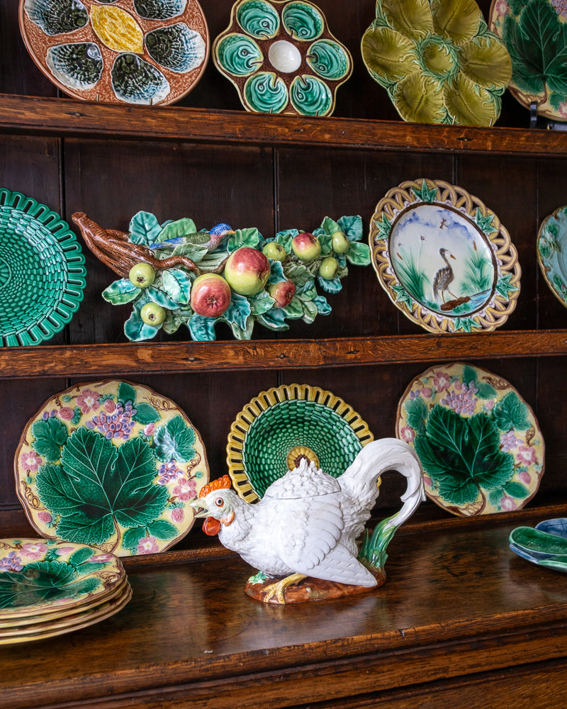 Collection of decorative ceramic plates and a teapot on a wooden shelf.