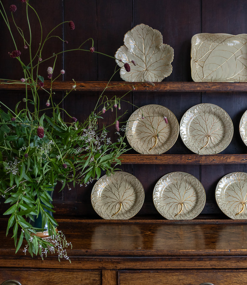 Antique Wedgwood plates with leaf patterns on a wooden dresser.