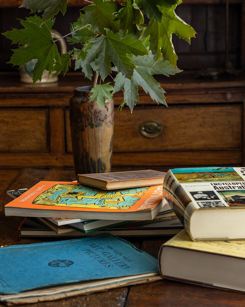 Stack of books on a wooden surface with a plant in the background