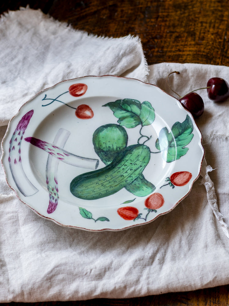 Antique Chelsea porcelain plate with cucumber and strawberry design on a rustic surface