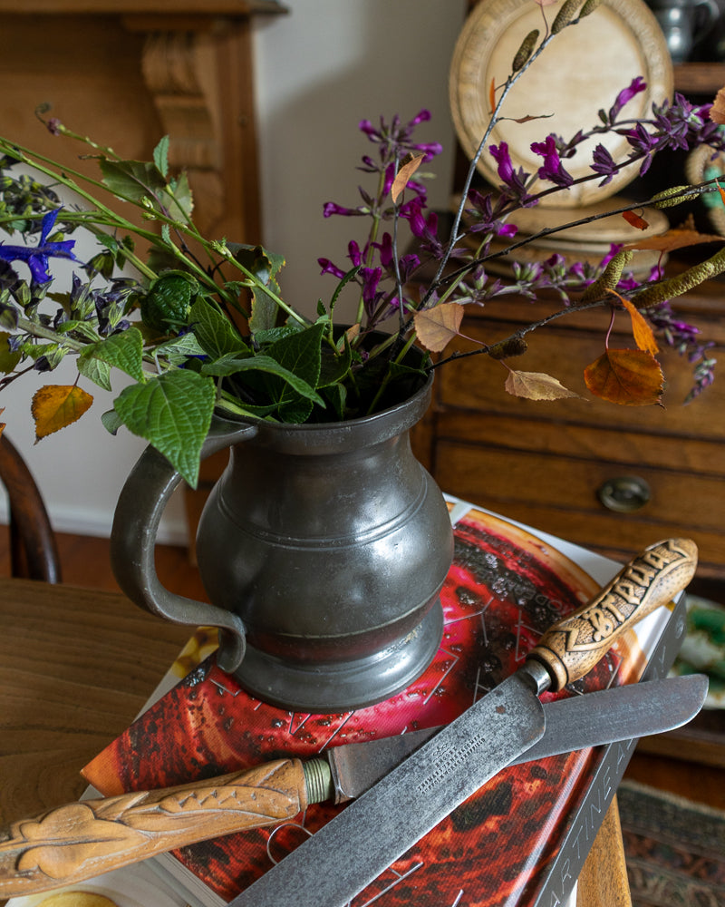 Decorative arrangement with a metal pitcher and flowers on a wooden surface.