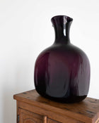 Glossy purple decanter on a wooden surface with a white background