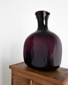 Glossy purple decanter on a wooden surface with a white background