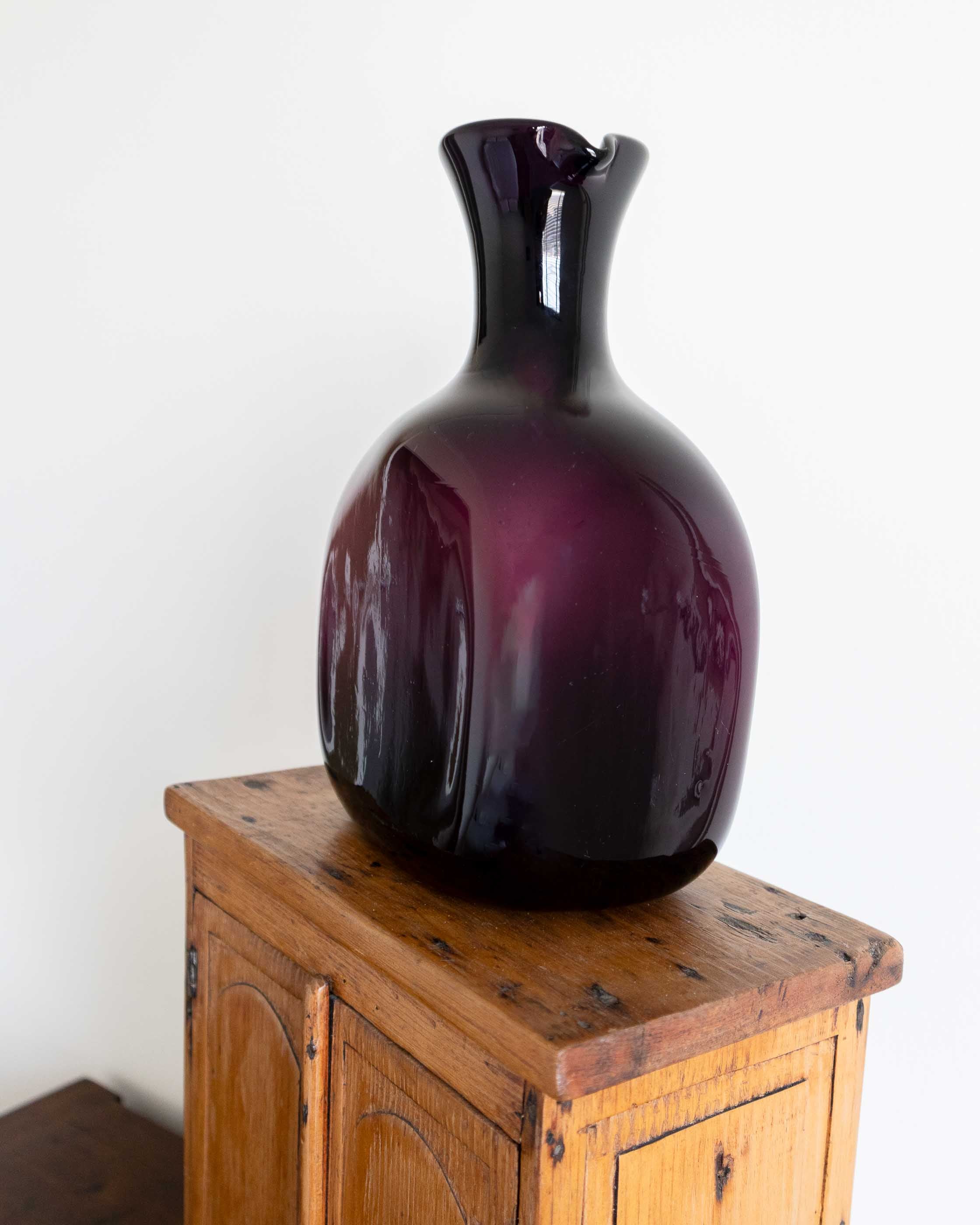 Purple decanter on a wooden cabinet against a white wall