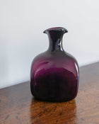 Purple glass decanter on a wooden surface with a white background