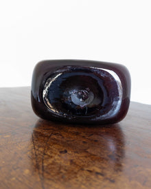 Dark glass object on a wooden surface with a white background