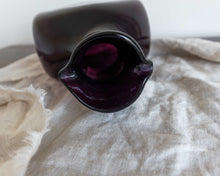 Dark purple glass decanter on a beige fabric surface