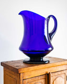 Blue glass pitcher on a wooden surface with a white background