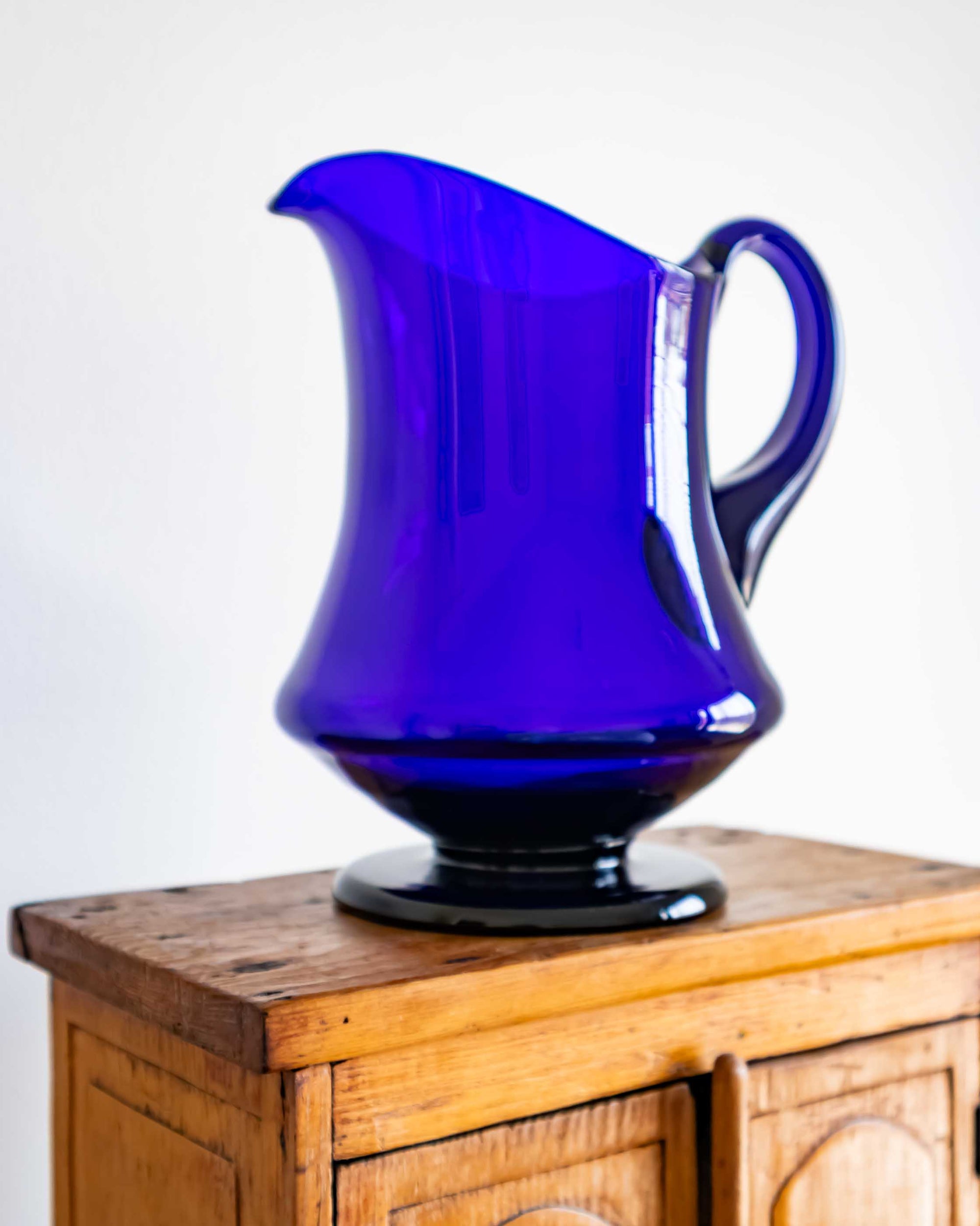 Blue glass pitcher on a wooden surface with a white background