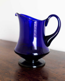 Blue glass pitcher on a wooden surface with a white background