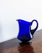 Blue glass pitcher on a wooden surface with a white background