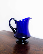 Blue glass pitcher on a wooden surface with a white background
