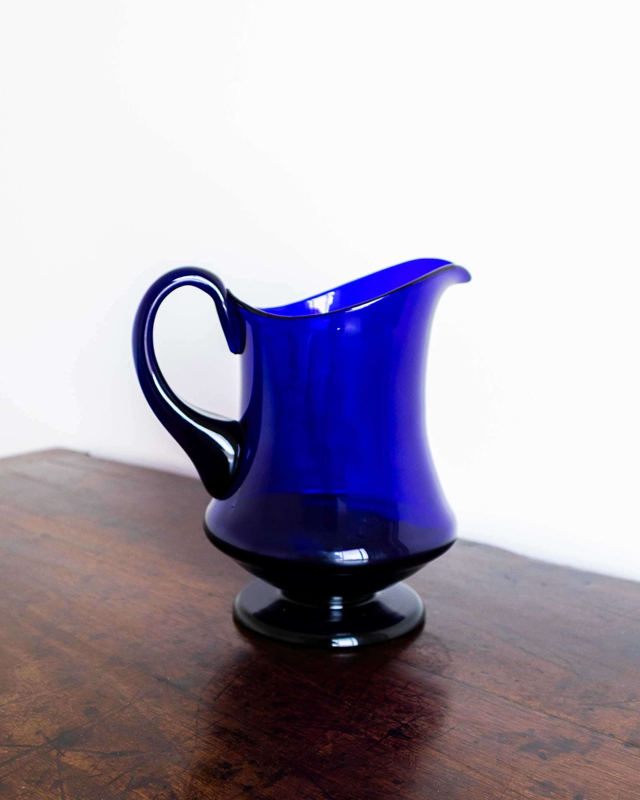 Blue glass pitcher on a wooden surface with a white background