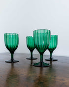 Four green glass goblets on a wooden surface with a light grey background
