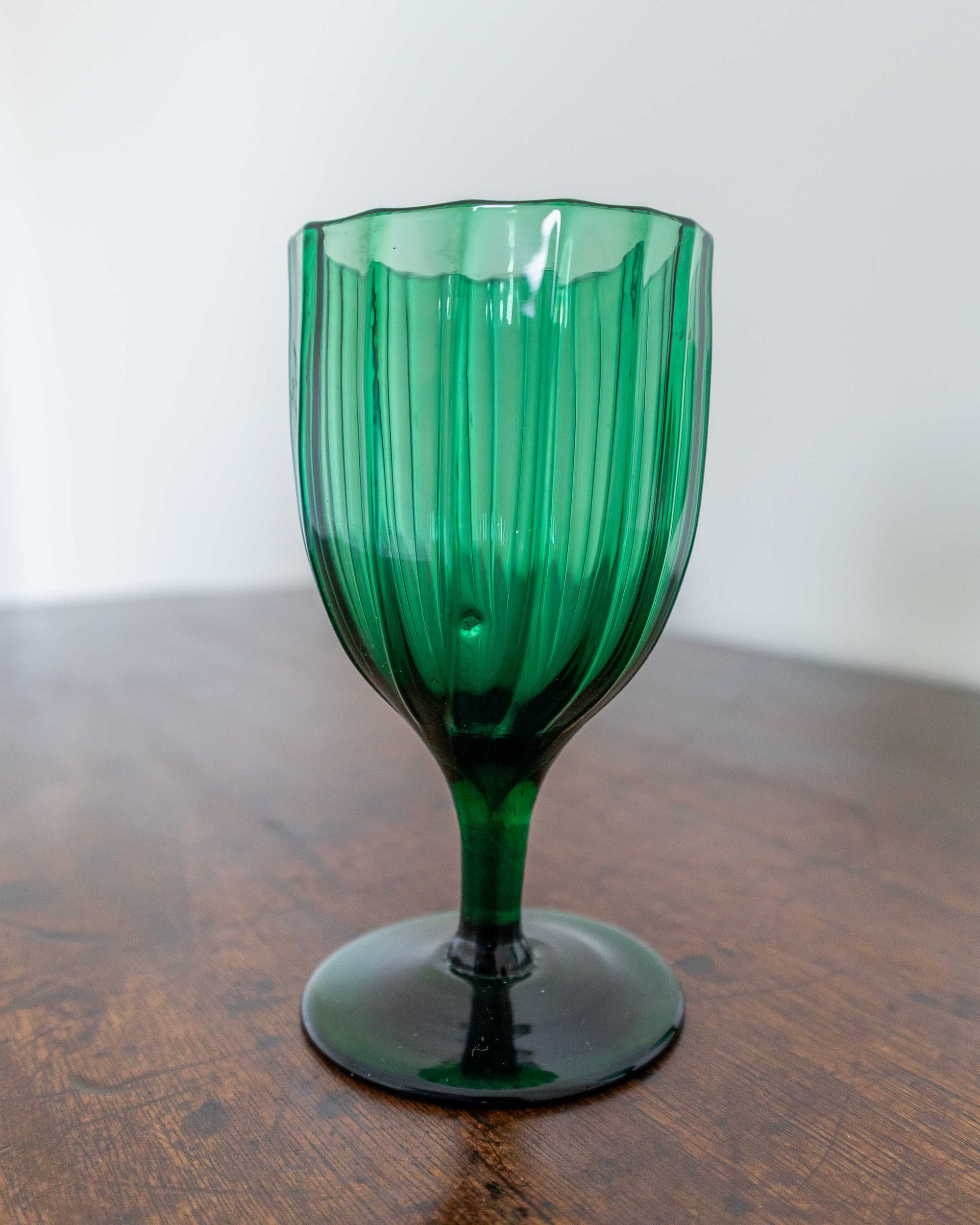 Green glass goblet on a wooden surface with a white background