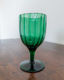 Green glass goblet on a wooden surface with a white background
