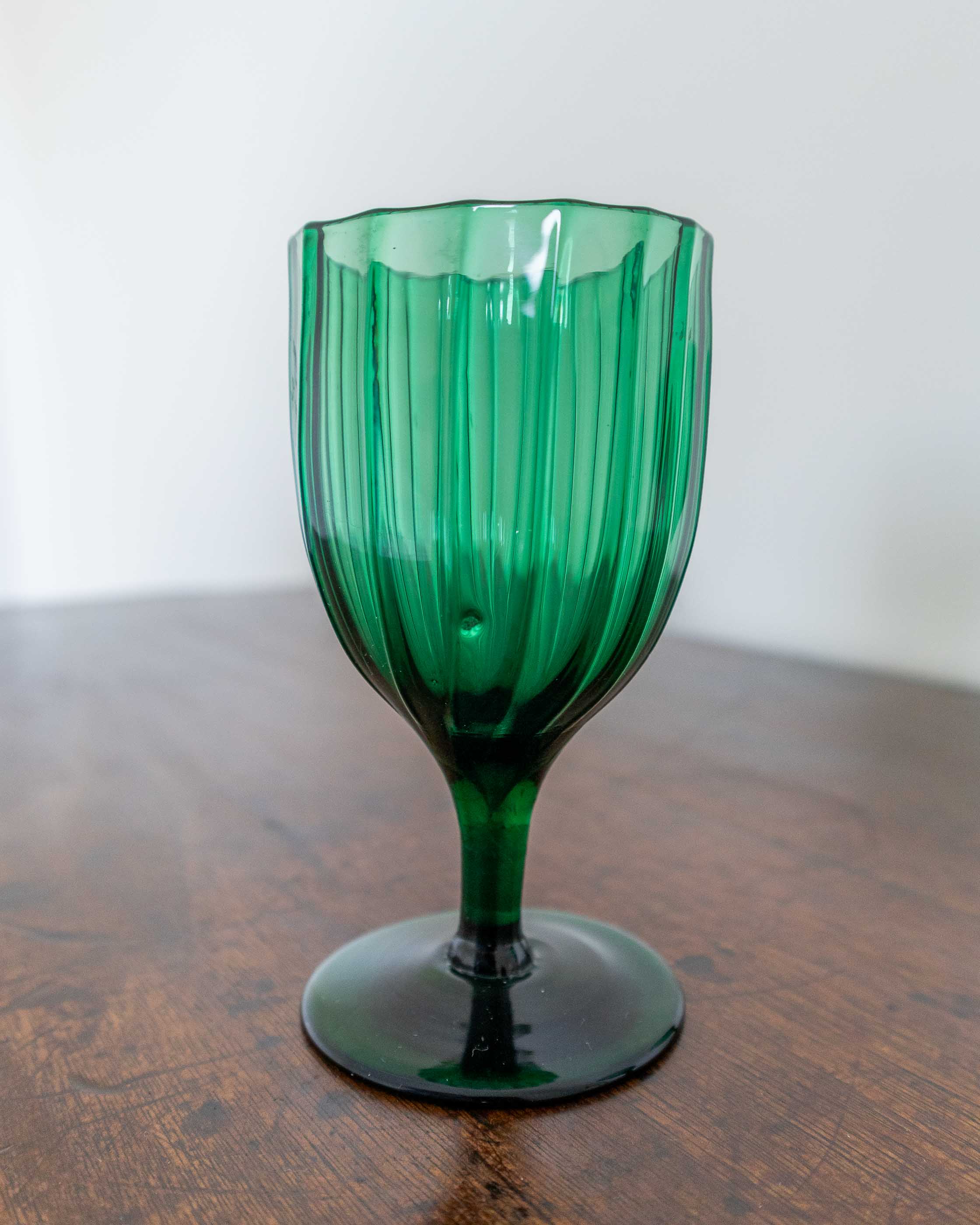 Green glass goblet on a wooden surface with a white background