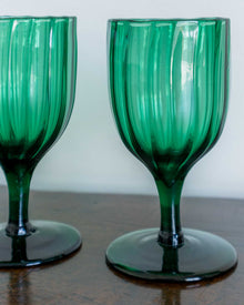 Two green glass goblets on a wooden surface with a white background