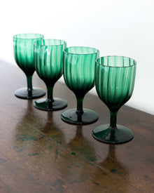 Four green glass goblets on a wooden surface with a white background