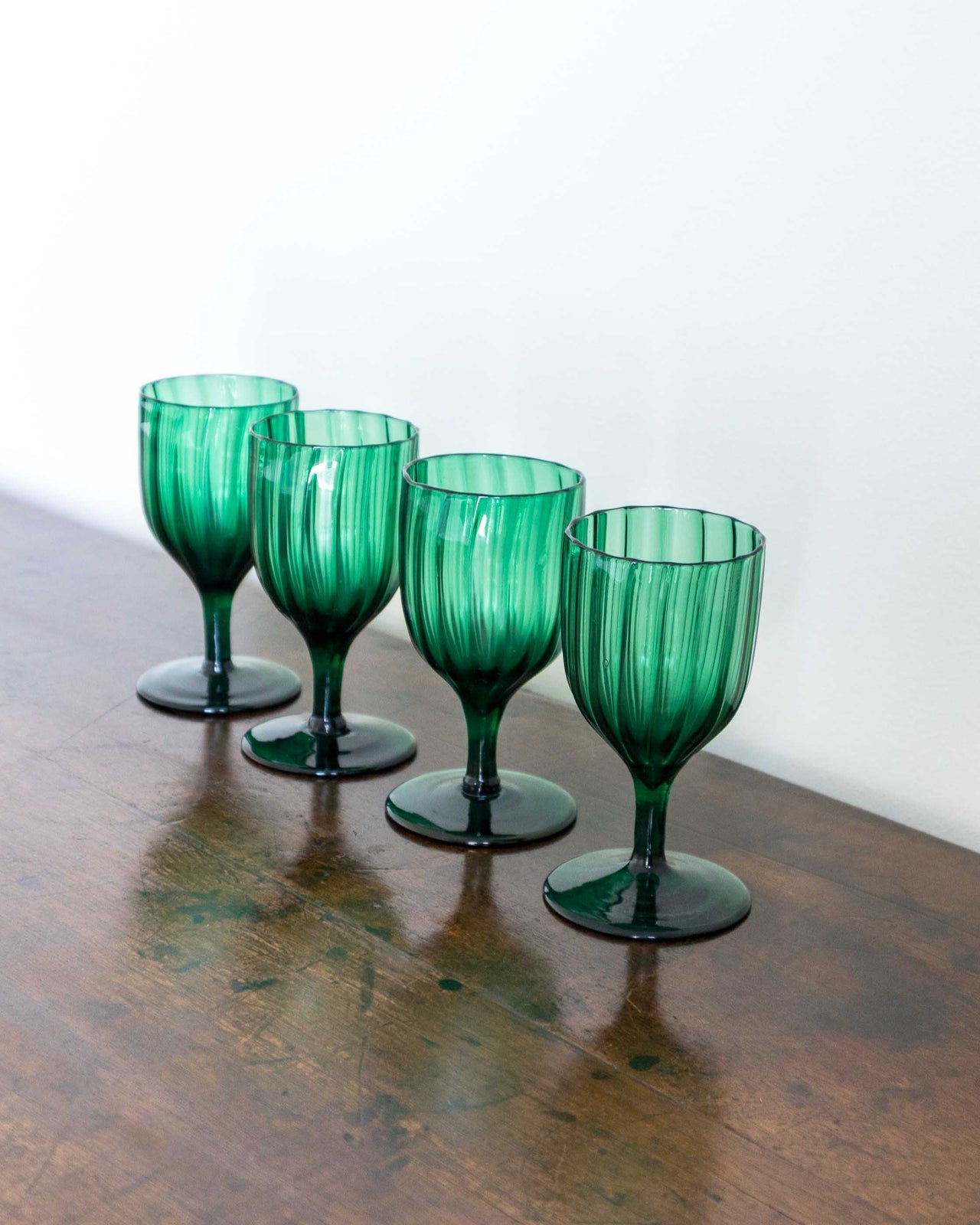 Four green glass goblets on a wooden surface with a white background