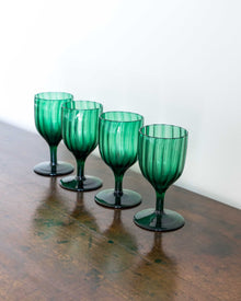 Four green glass goblets on a wooden surface with a white background