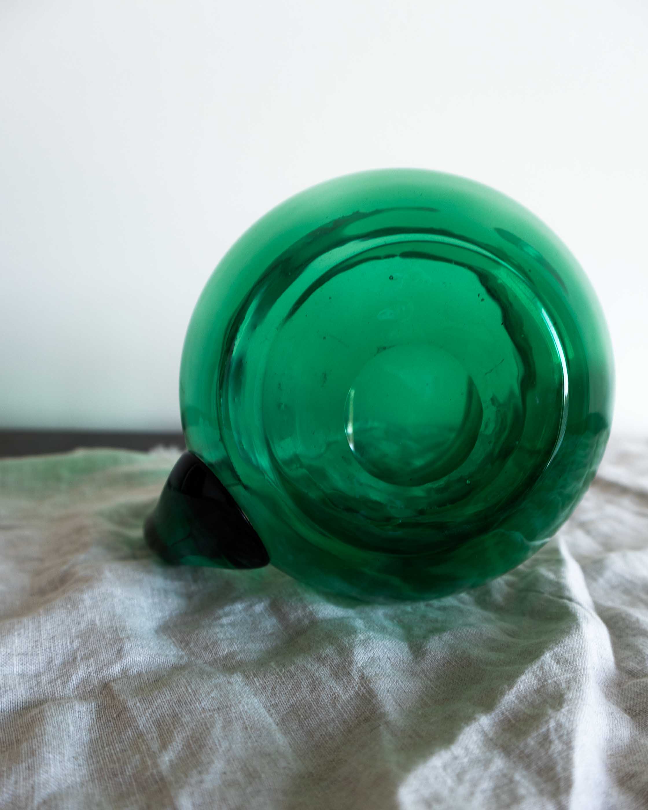 Green glass jug on a white fabric surface